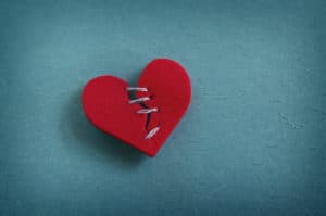 A red felt heart that is broken and stitched up loosely with thread.