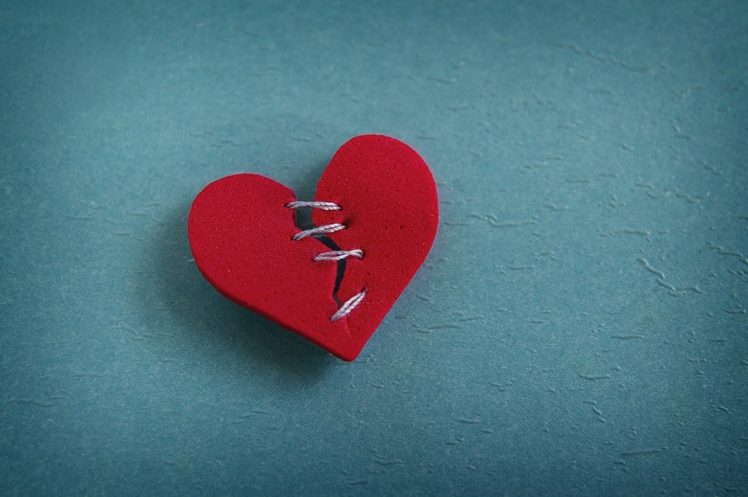 A red felt heart that is broken and stitched up loosely with thread.