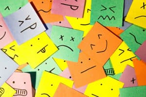 A scattered pile of colorful sticky notes with different facial expressions drawn on them.