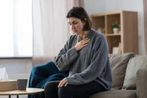 Woman sits on the sofa hand over her heart working through an anxiety attack.