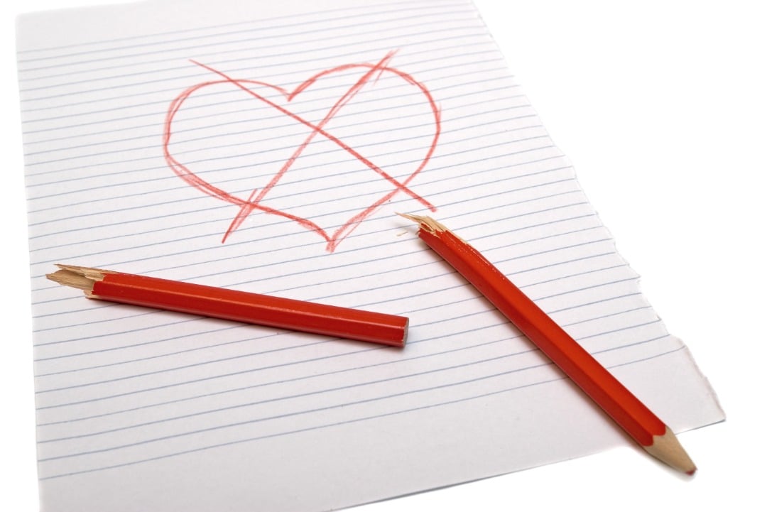 Notebook paper with a heart drawn on it in red pencil. The heart has an "x" through it and the red pencil is broken in half.